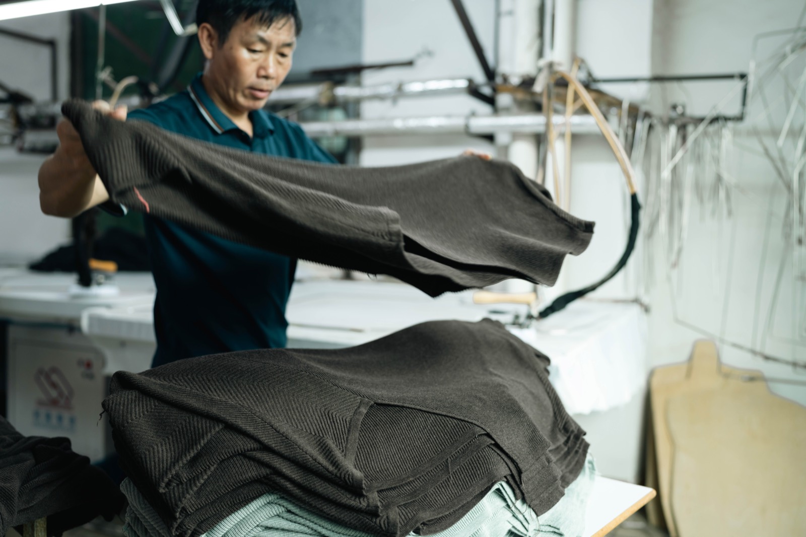 Operator folding a pressed brown knitted garment onto a stack at the pressing table
