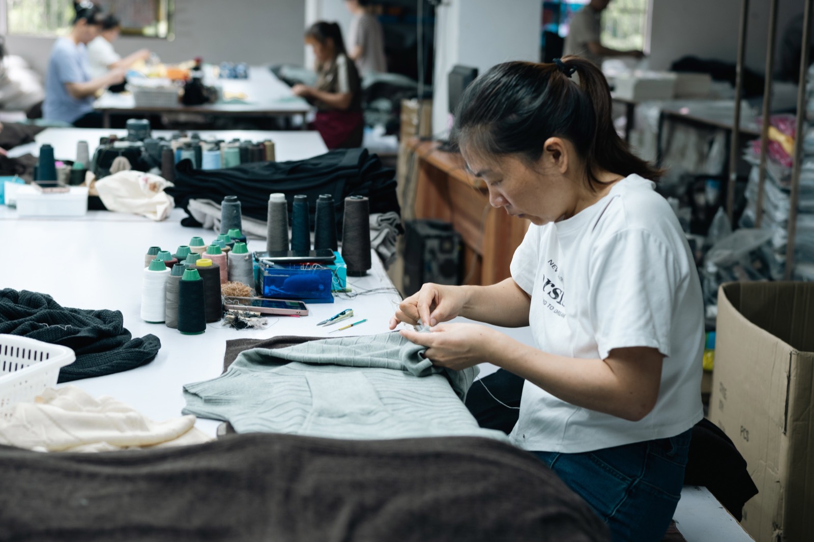 Operator hand-finishing a grey knitted garment at a work table