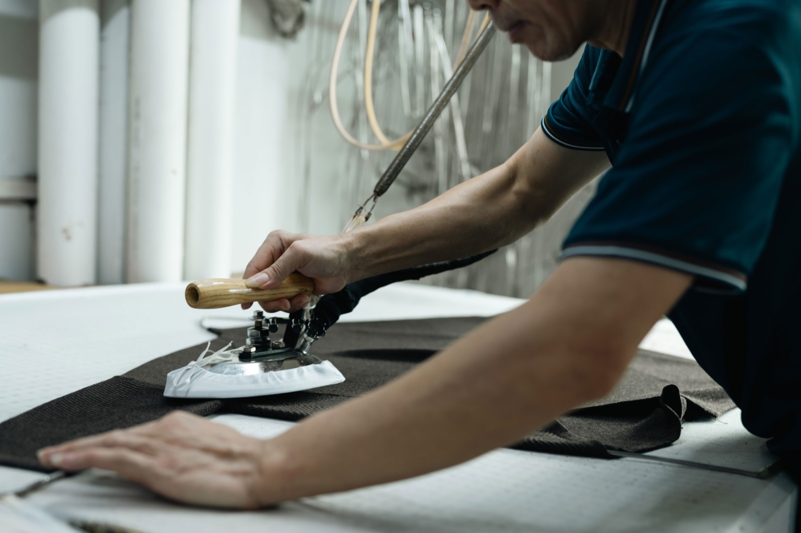 Operator steam-pressing a brown knitted panel on a pressing table