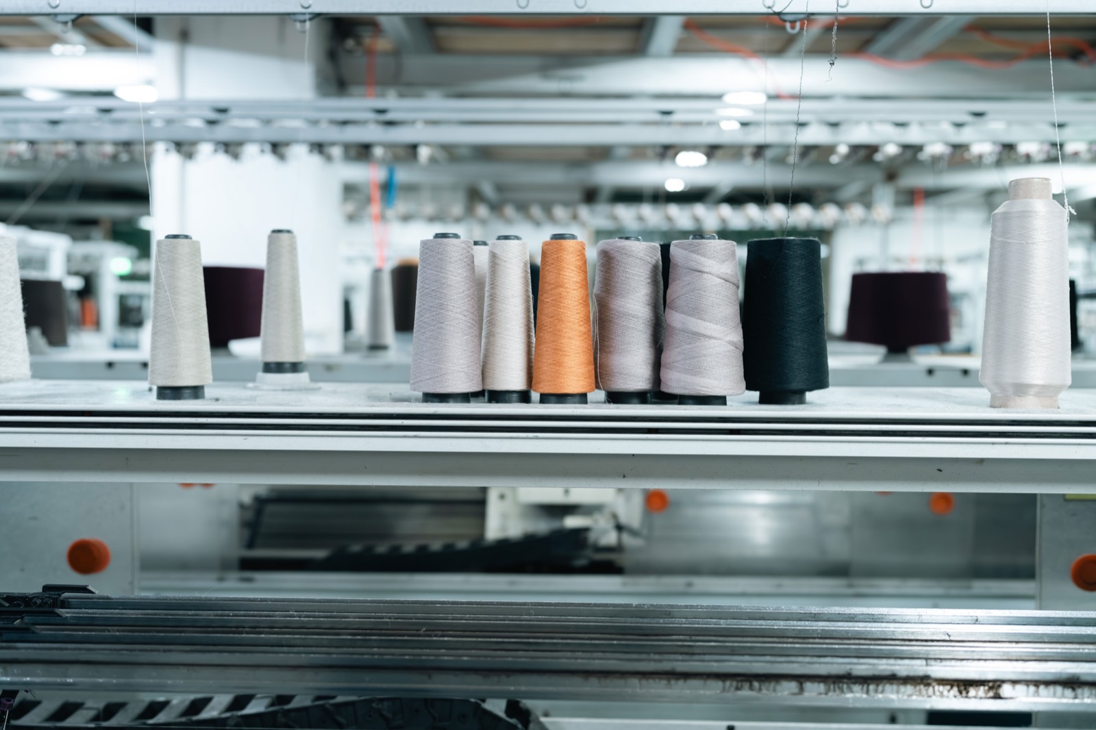 Cones of cream, orange and burgundy yarn on the creel above a knitting machine